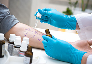 a person's arm with a numbered grid drawn on it while a medical professional tests allergens on their skin